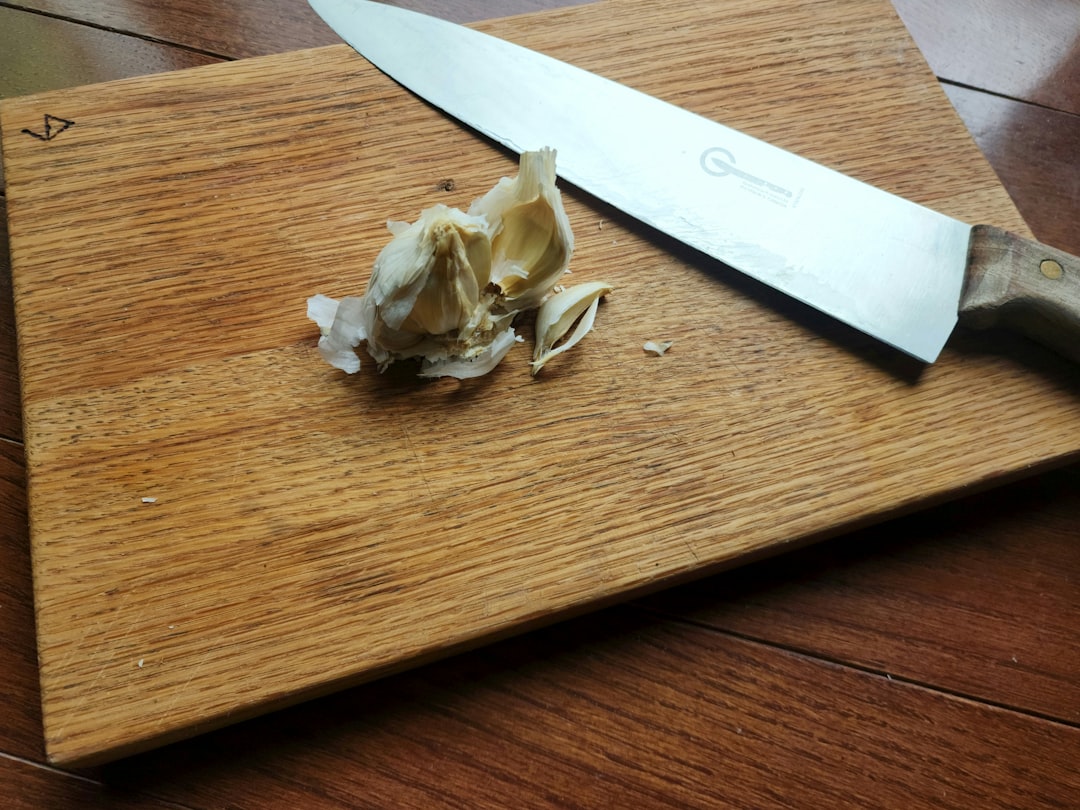 Peeled garlic and a knife on a wooden cutting board