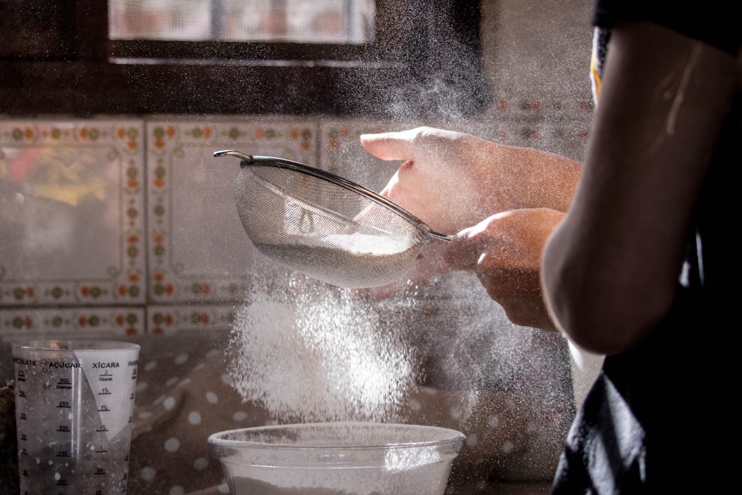 Hands sifting flour through a sieve into a bowl