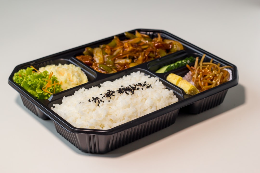 Compartmentalized bento lunch box filled with rice, vegetables, fruit, and protein