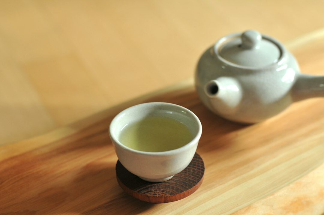 A cup of green tea beside a ceramic teapot on a wooden surface