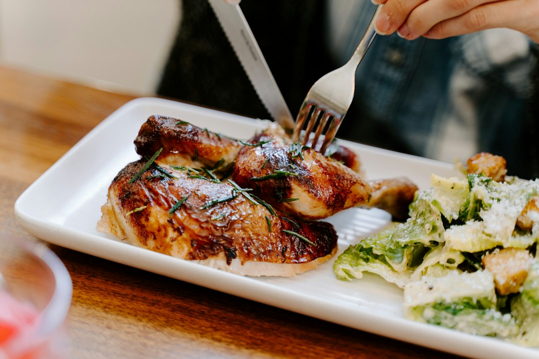 Hands carving roasted chicken with a fork on a white plate