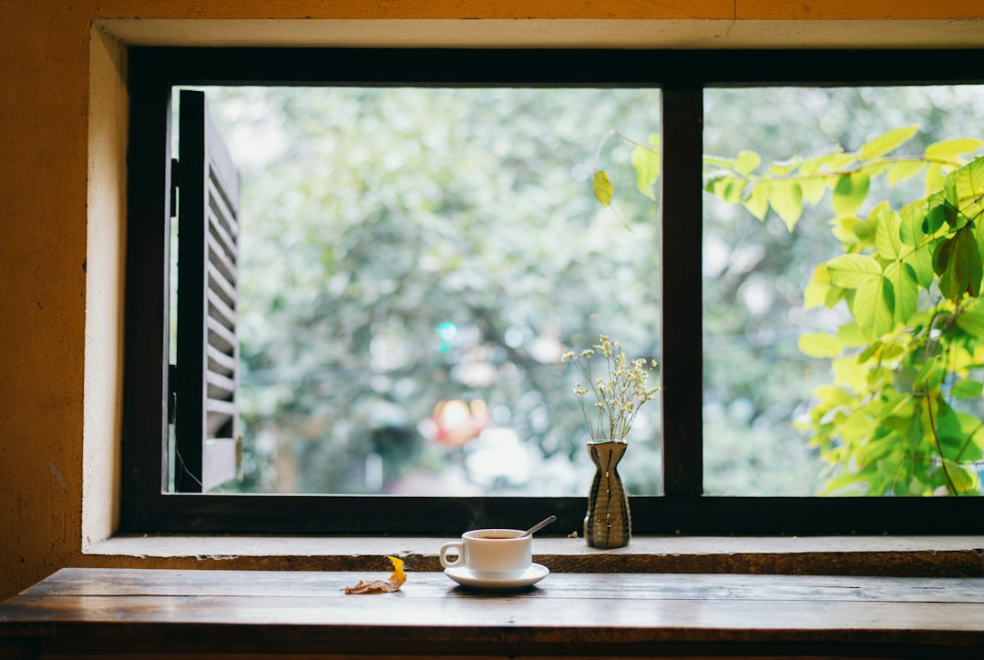 A steaming cup of tea on a wooden windowsill beside fresh flowers