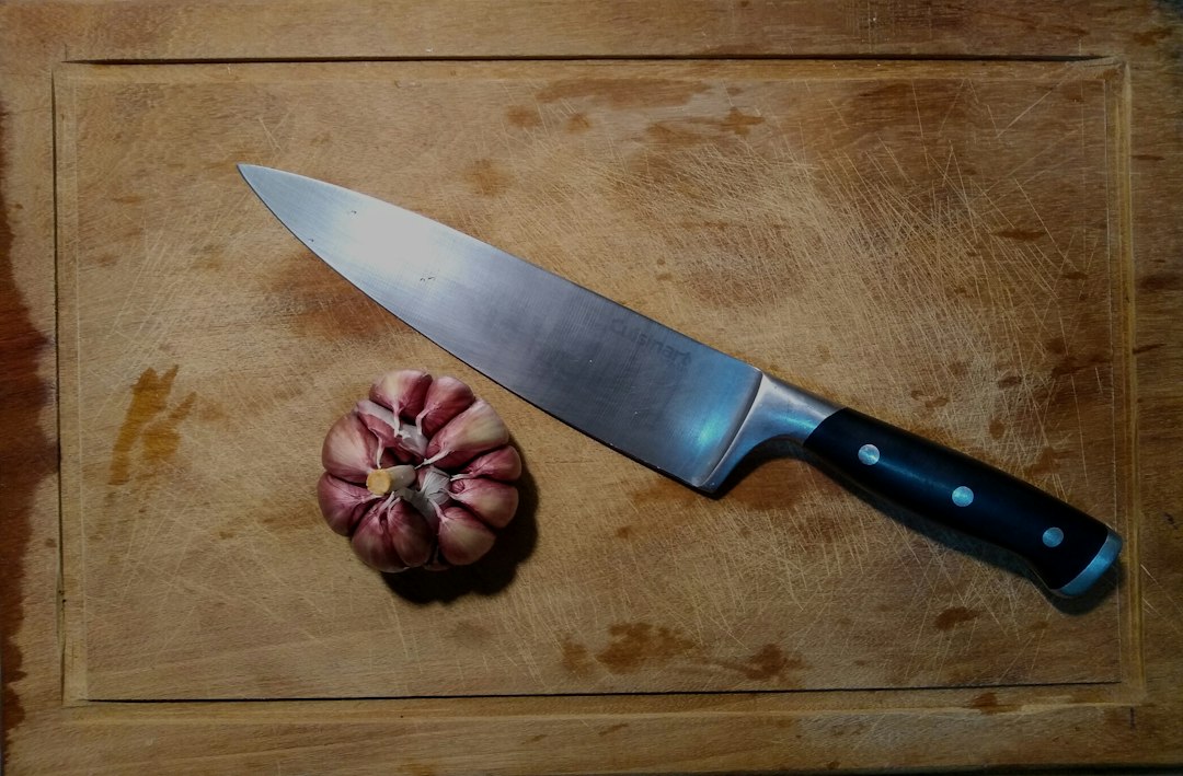 A chef's knife and garlic bulb on a cutting board for smashing and peeling