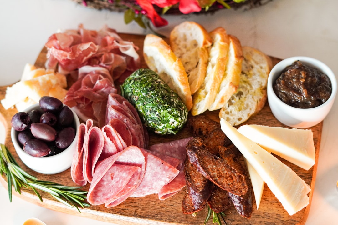 A long wooden board crowded with cured meats, cheeses, bread and olives for a raclette or fondue table