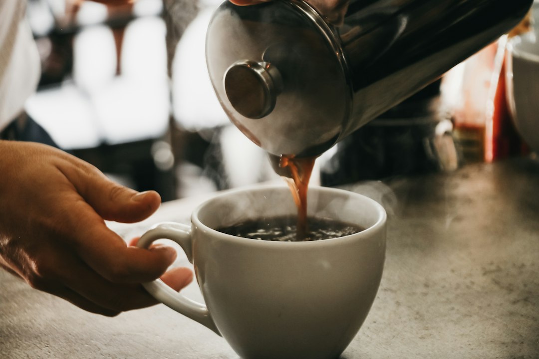 Coffee pouring from a French press into a mug with steam rising