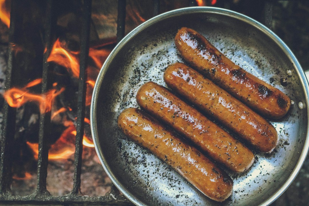 Bratwursts sizzling in a pan over an open flame