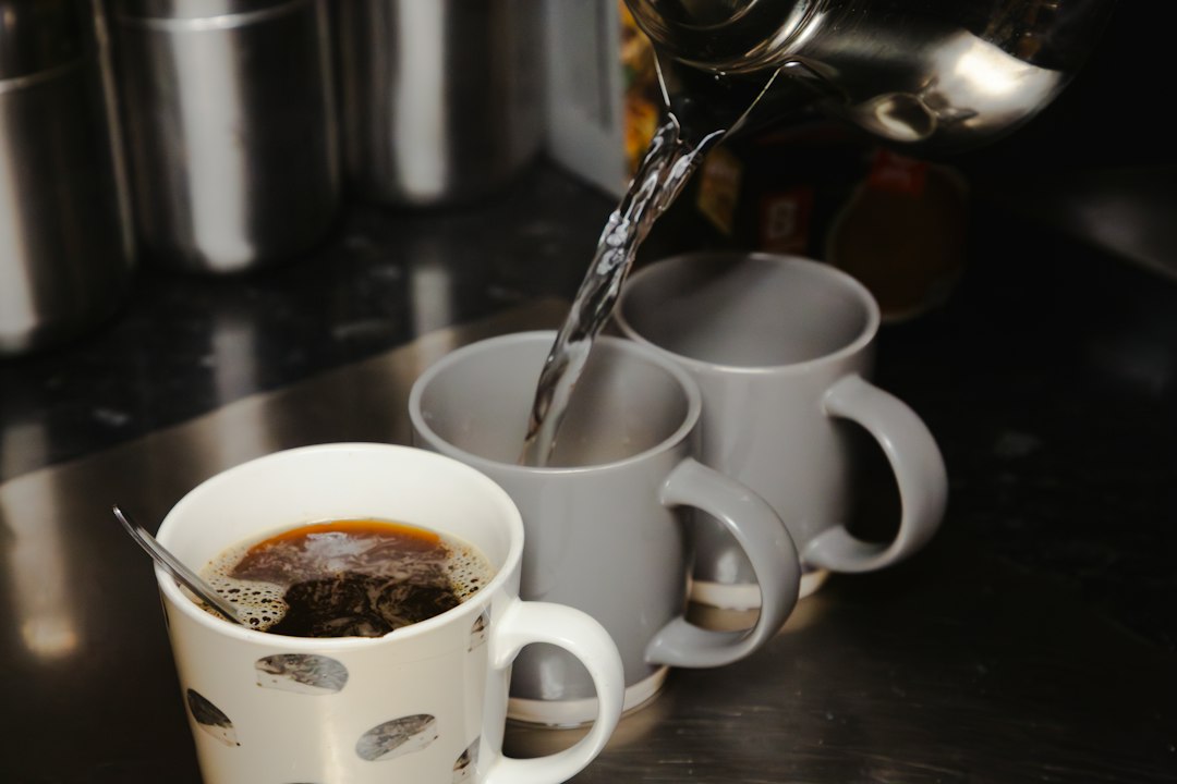 Hot water pouring from a kettle into mugs on a dark countertop