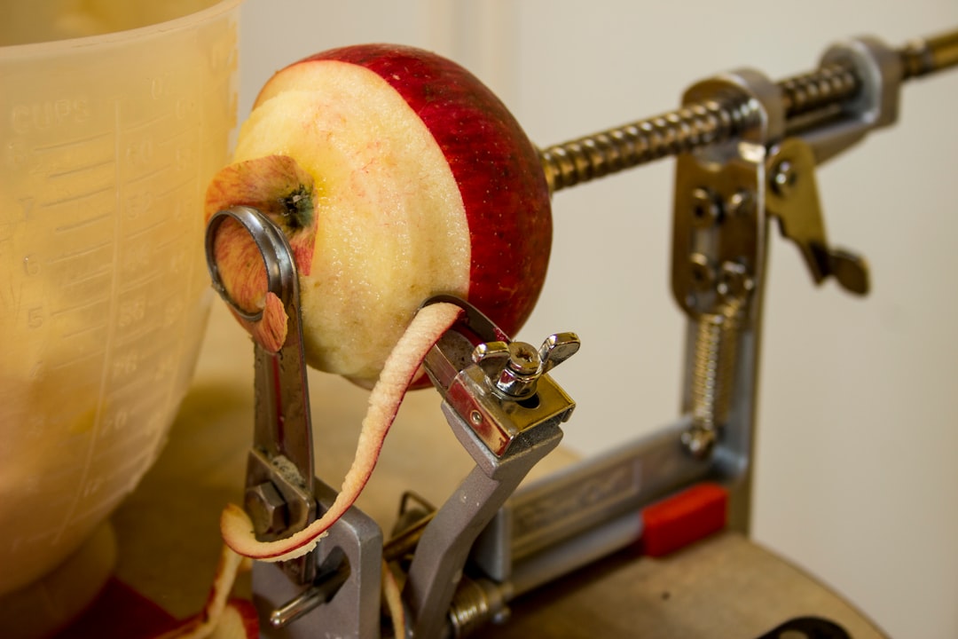 A red apple being peeled by a hand-crank apple peeler on a kitchen counter