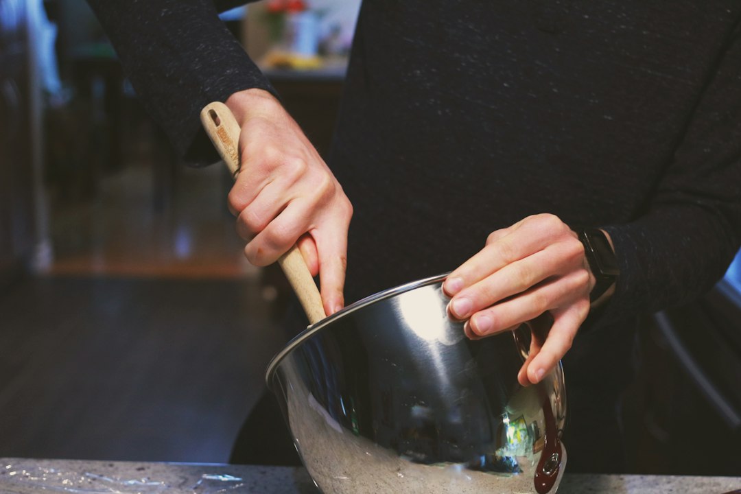 Hands mixing batter in a stainless steel mixing bowl