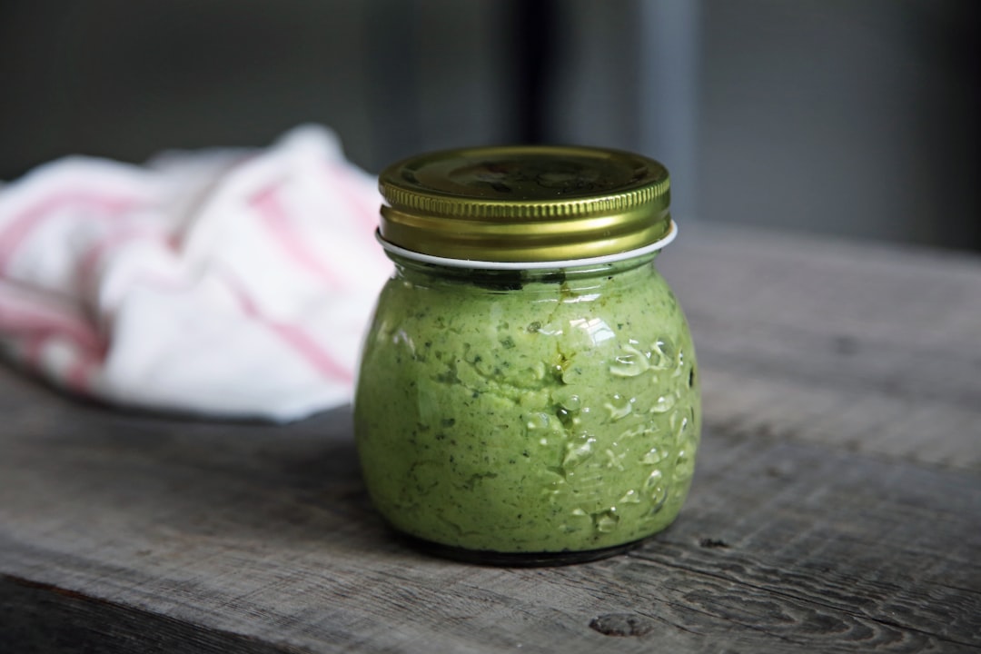 A glass jar of fresh green basil pesto on a wooden board