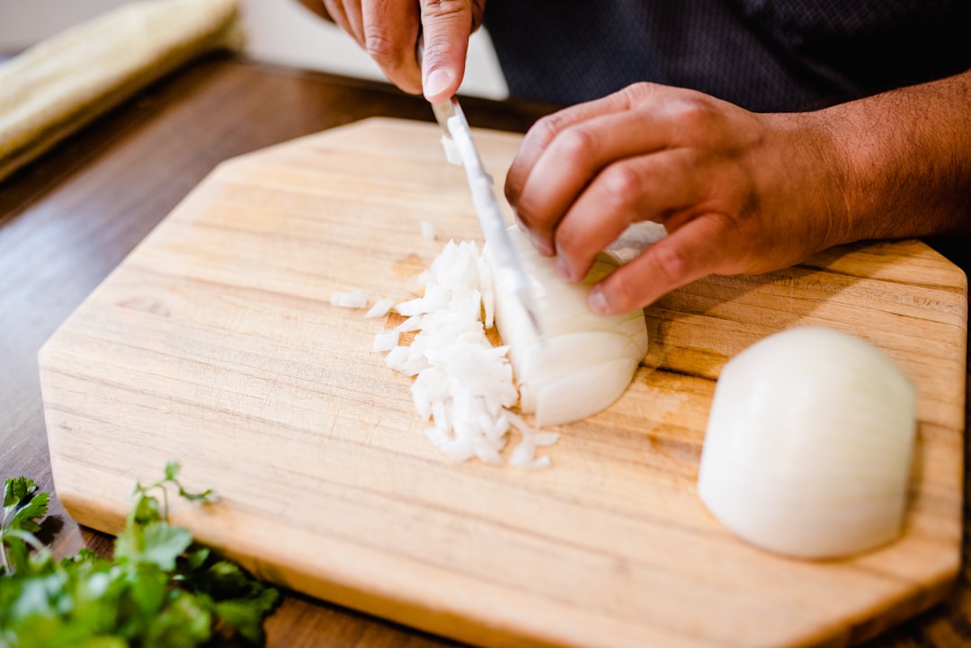 Hands chopping onions on a wooden cutting board