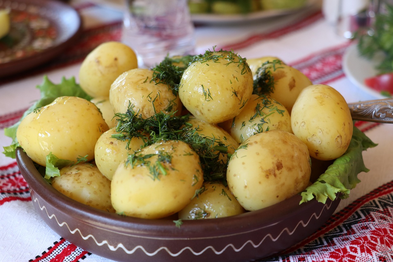 A brown ceramic bowl of buttery baby potatoes with fresh chopped dill on an embroidered tablecloth