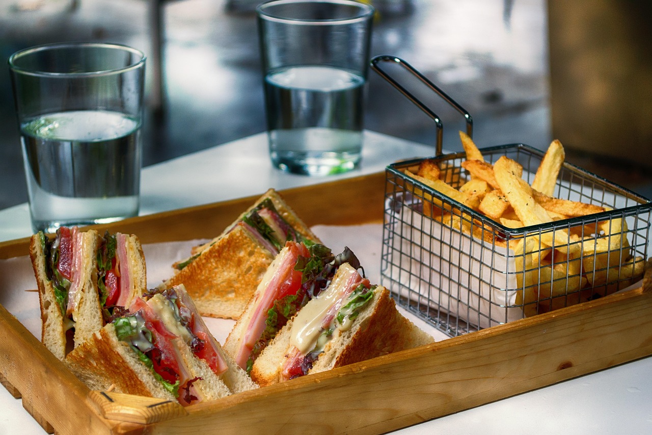 Golden French fries in a small wire fry basket beside toasted club sandwiches