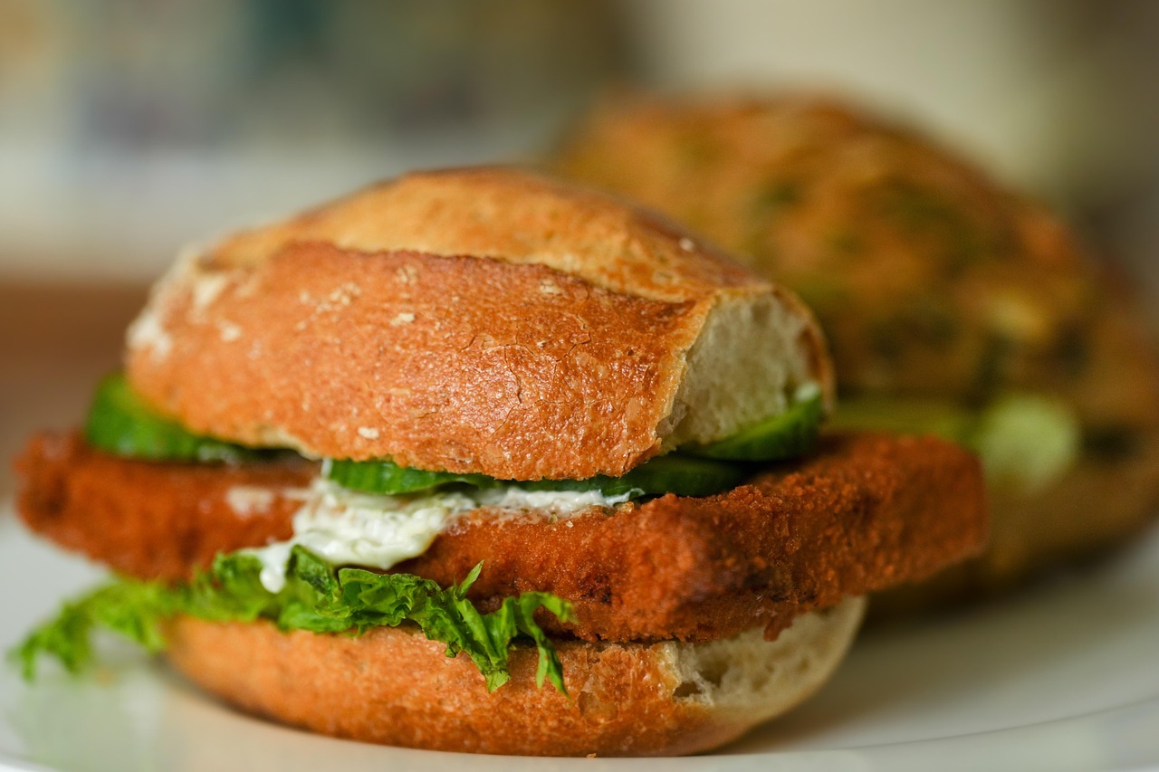 A golden fried fish fillet sandwich with lettuce, cucumber, and tartar sauce on a crusty roll