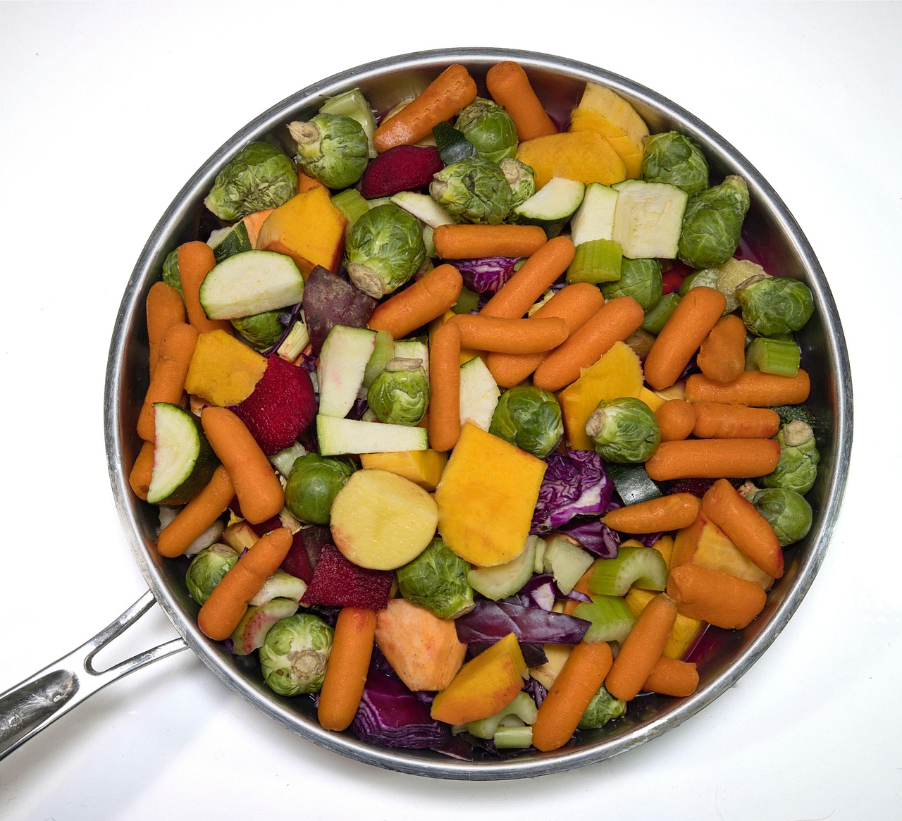 A polished stainless steel skillet heaped with chopped fall vegetables ready to roast