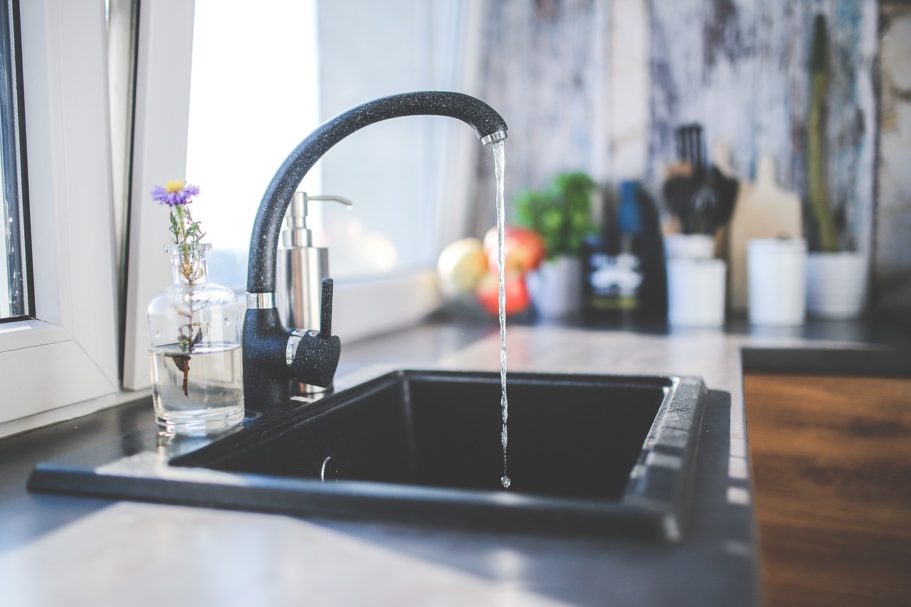 Cold water running from a black kitchen faucet into a dark sink for a cold-water turkey thaw