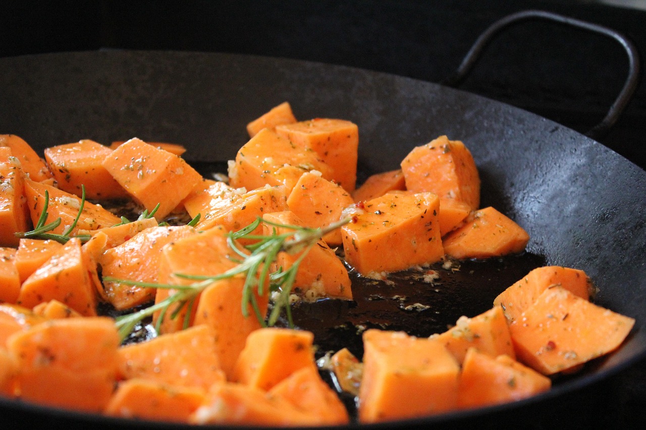 Cubed sweet potatoes tossed with olive oil, garlic, and fresh rosemary sprigs in a dark pan