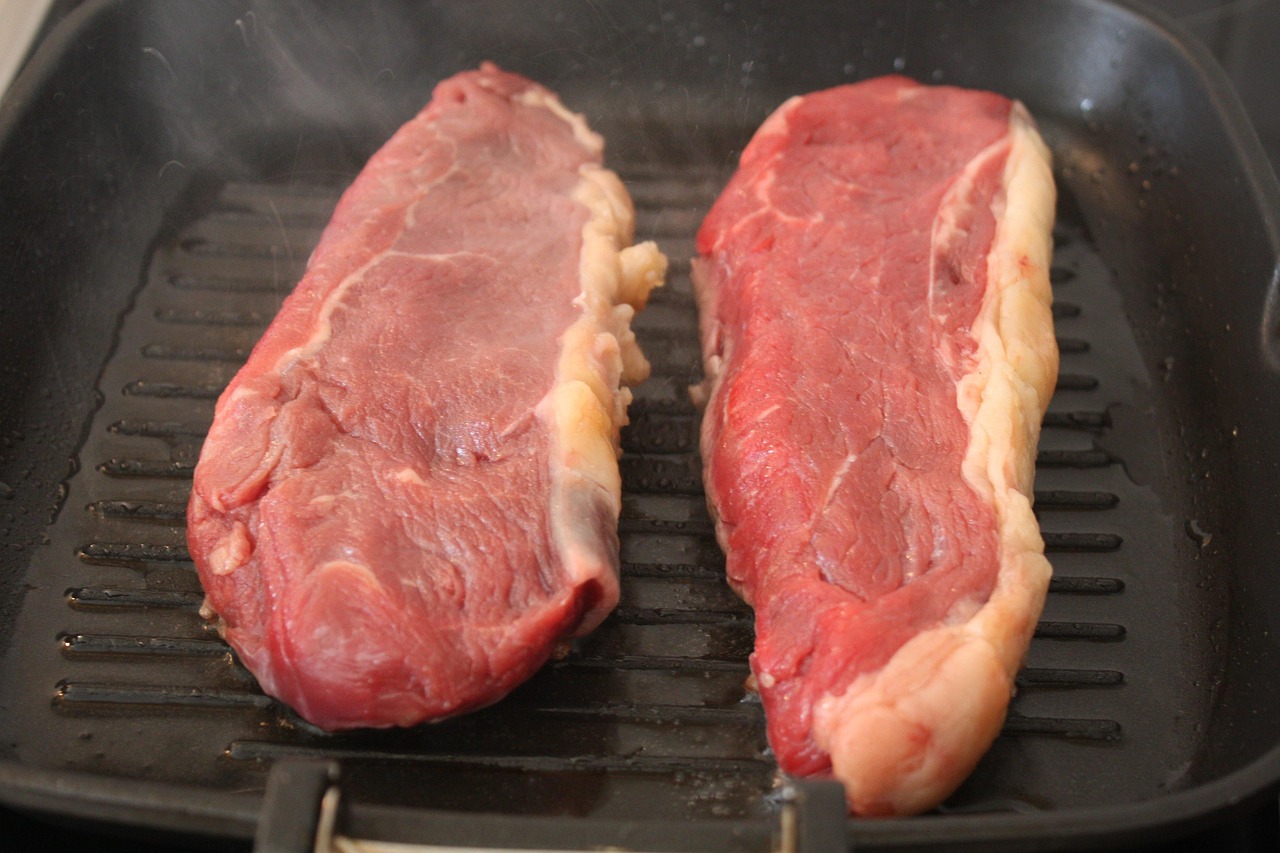 Two strip steaks going into a hot pan for a hard sear