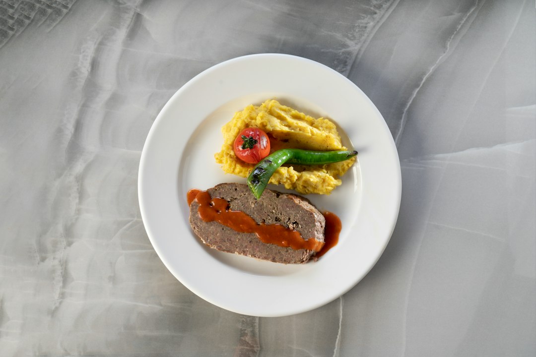 White plate holding a slice of meatloaf with red sauce and a scoop of mashed potatoes