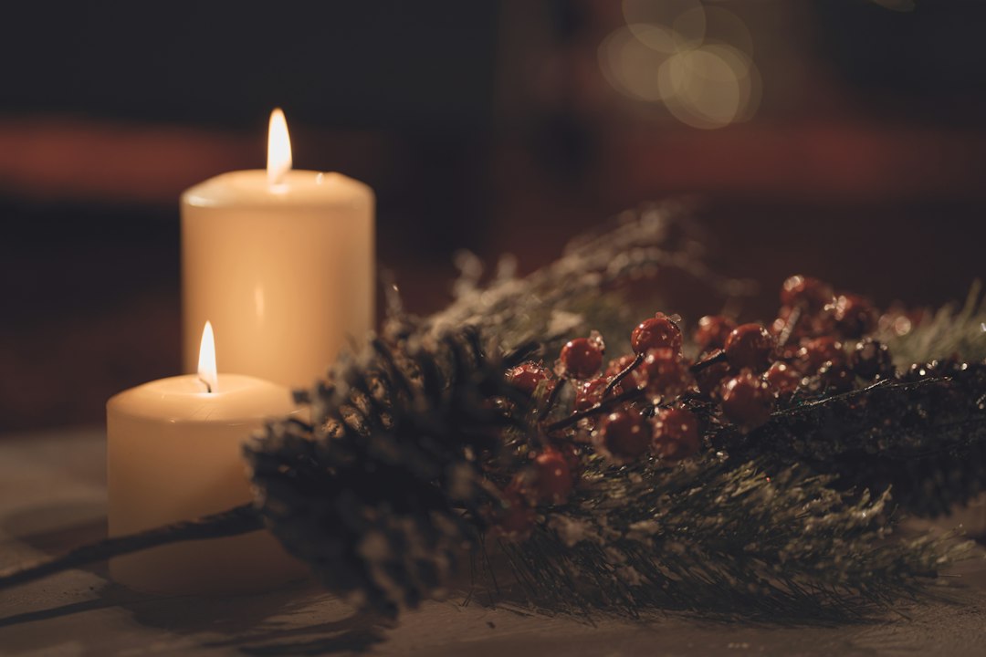 Lit pillar candles beside frosted pinecones and red berries in a festive arrangement
