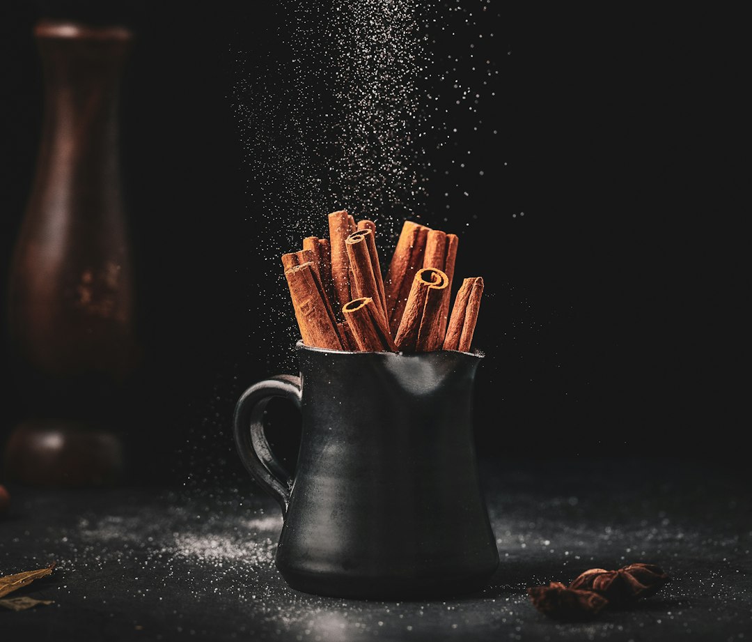 Cinnamon sticks in a small pitcher with sugar falling around them