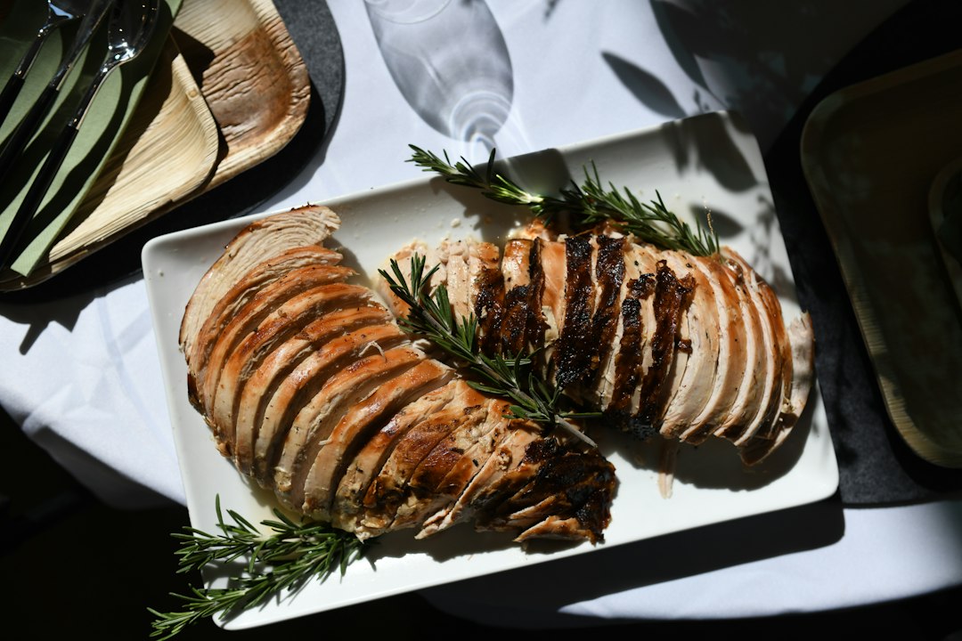 Thin slices of roasted turkey breast arranged on a white platter with rosemary