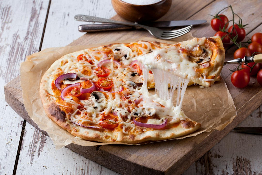 A tomato and mushroom pizza with a slice lifted and melted mozzarella stretching