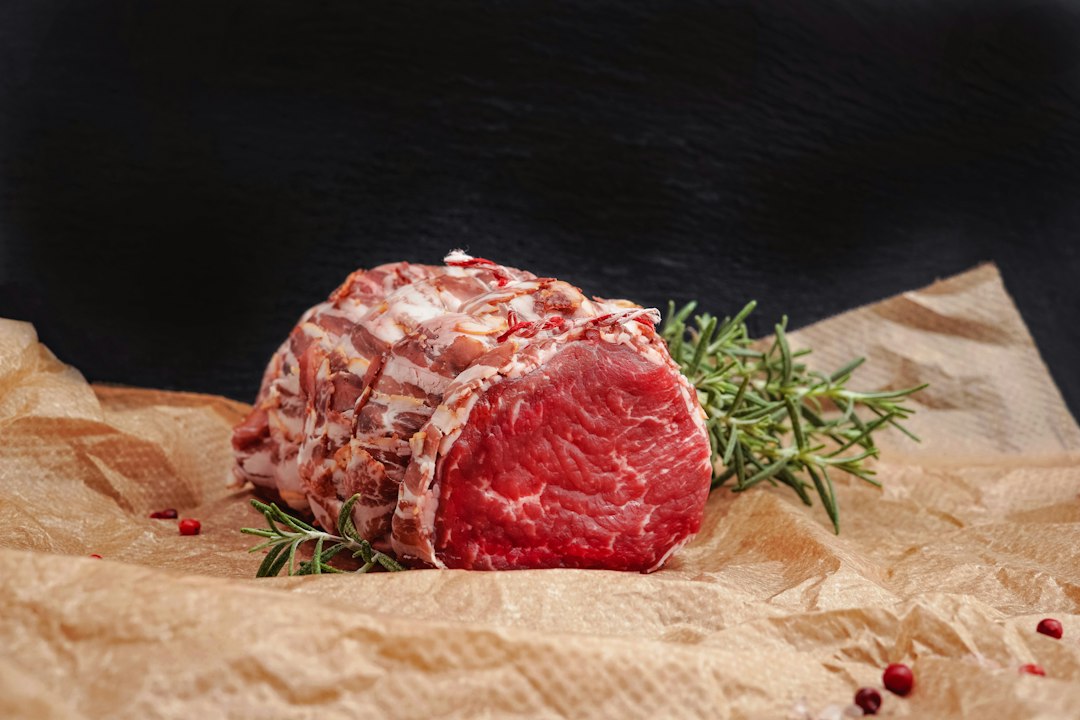 A raw roast tied with butcher twine and bacon on brown paper, rosemary beside it