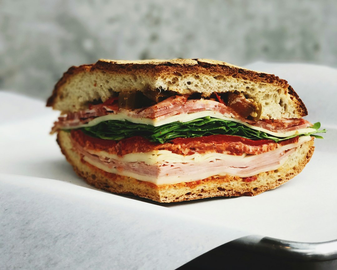 Hearty sandwich on crusty bread stacked with deli meats, cheese, greens, and tomato