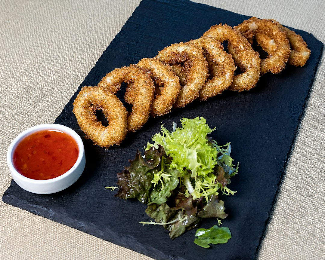 Golden panko-crusted fried rings on a slate board with a sweet chili dip and greens