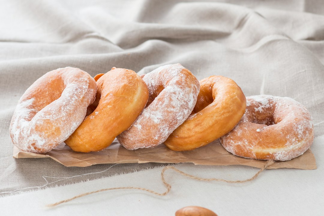 A row of homemade doughnuts, some dusted with powdered sugar, on brown parchment and linen