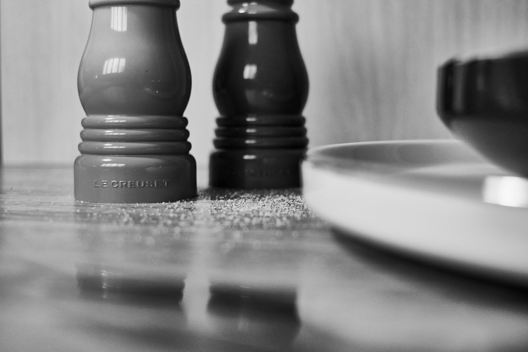 Two salt and pepper mills on a wooden counter with scattered grains