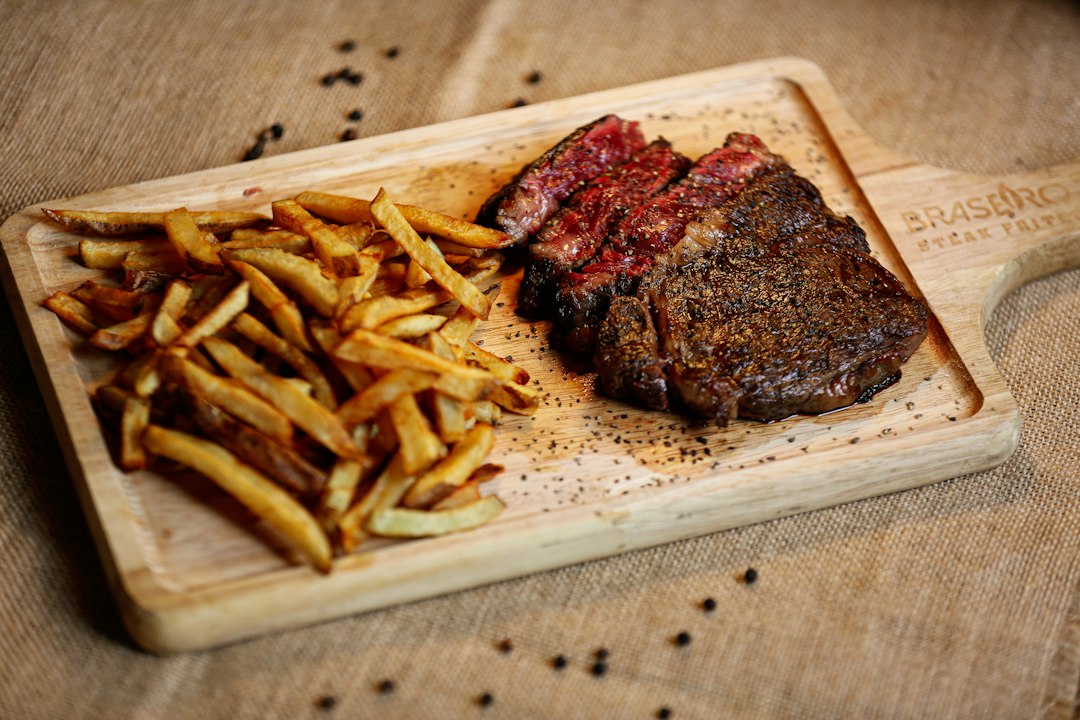 Steak with cracked pepper crust beside scattered peppercorns