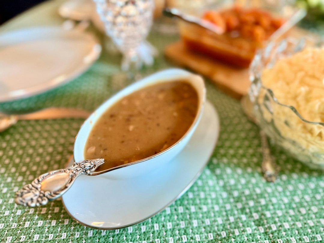 A white gravy boat filled with peppered gravy and a silver ladle, sitting on a set table