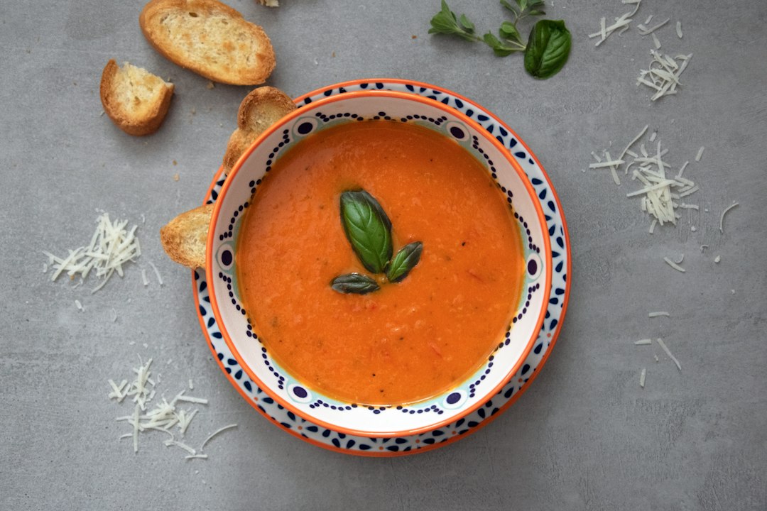 Bowl of tomato soup with fresh basil, shredded cheese, and toasted bread slices for dunking