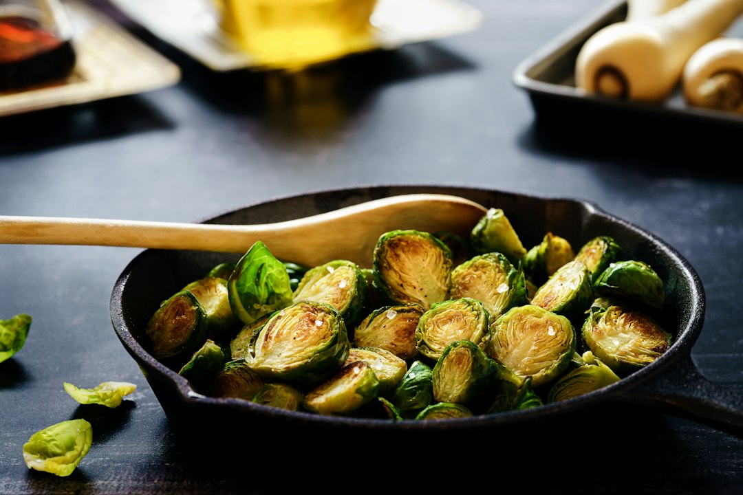Halved Brussels sprouts browned and caramelized in a small black skillet with a wooden spoon