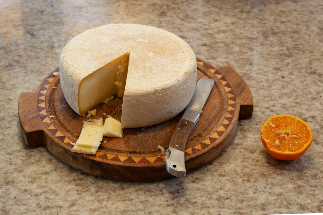 A round aged cheese wheel with a cut wedge and a knife on a wooden board