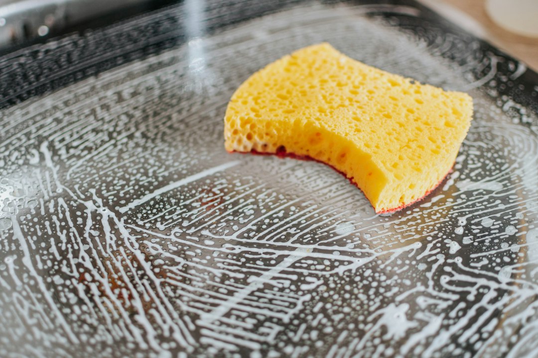 A yellow sponge scrubbing soapy water across a stainless steel pan
