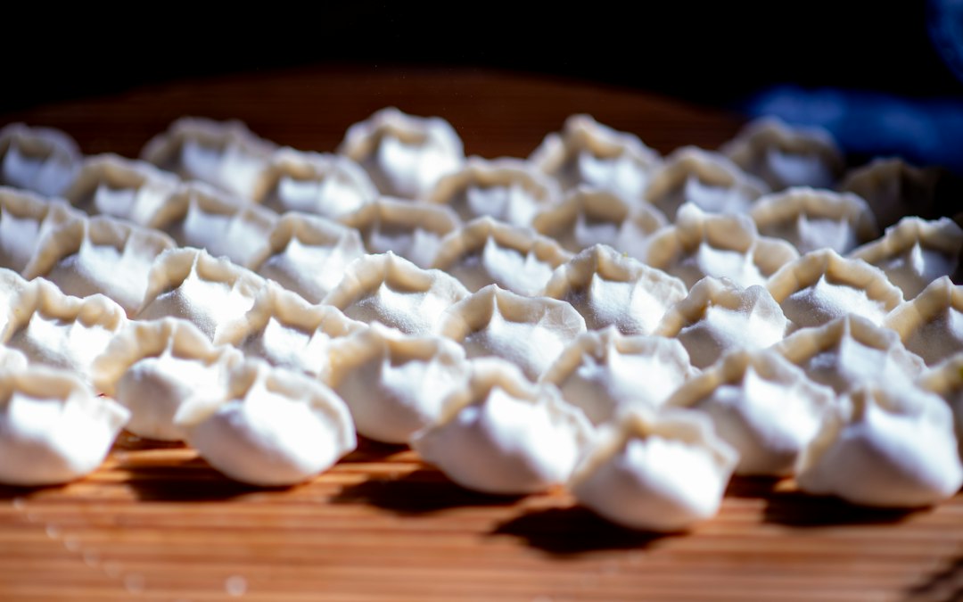 Rows of uncooked pleated dumplings on a wooden board