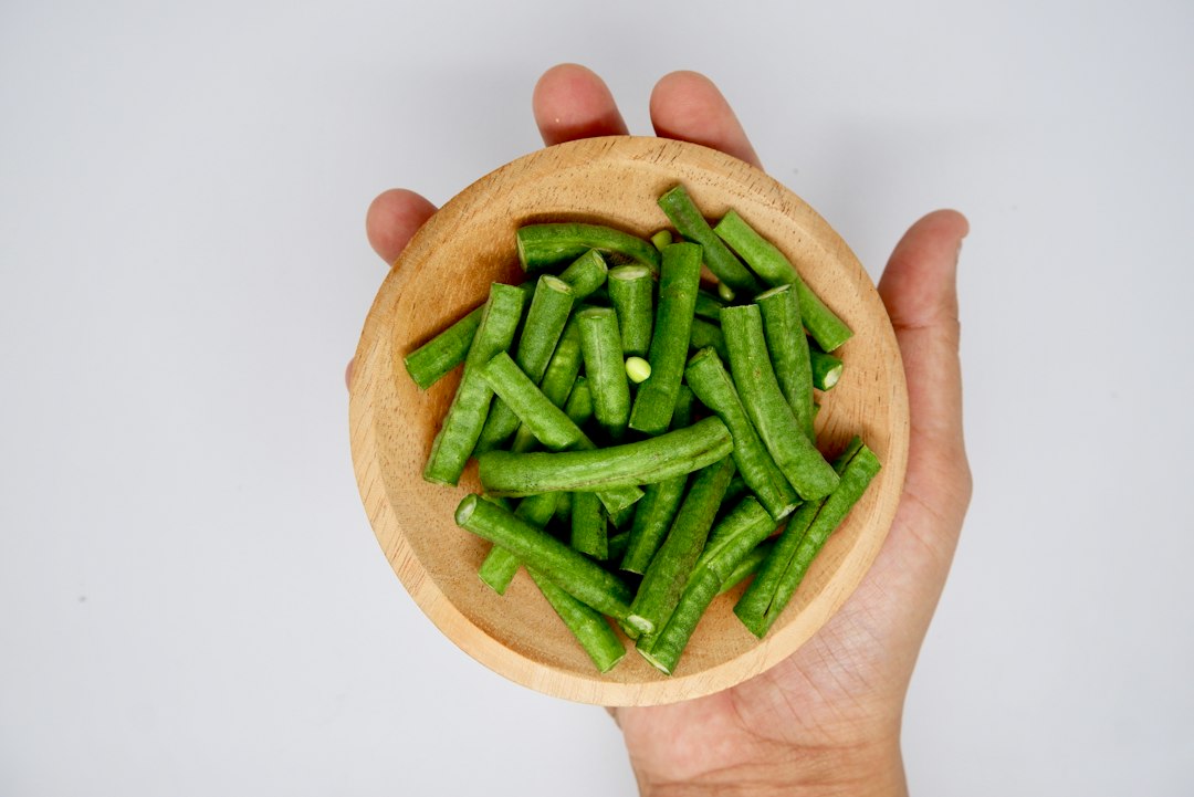 Cut green beans in a small wooden bowl held in one hand