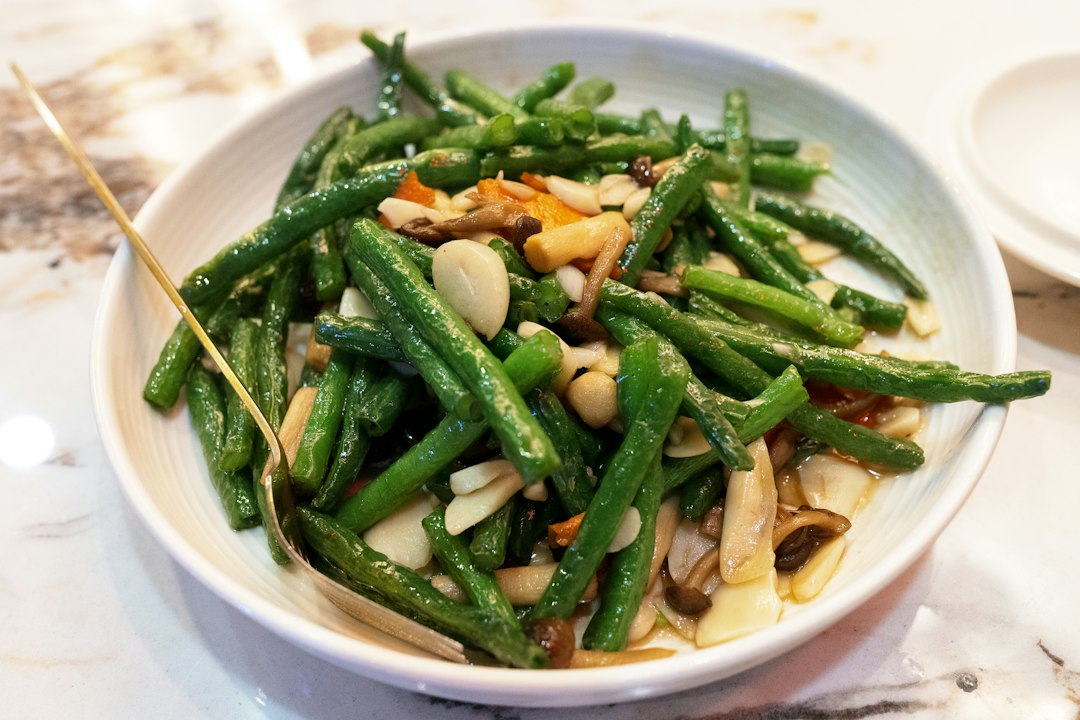 A white bowl of blistered green beans with sliced garlic and mushrooms on a marble countertop