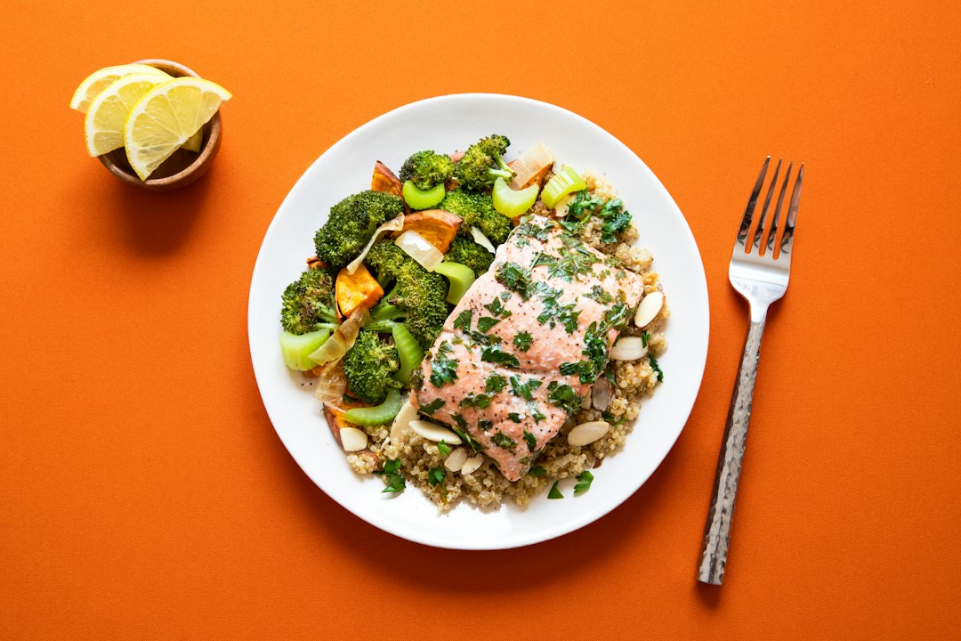 Herb-flecked salmon fillet with broccoli, grains, and lemon on a white plate