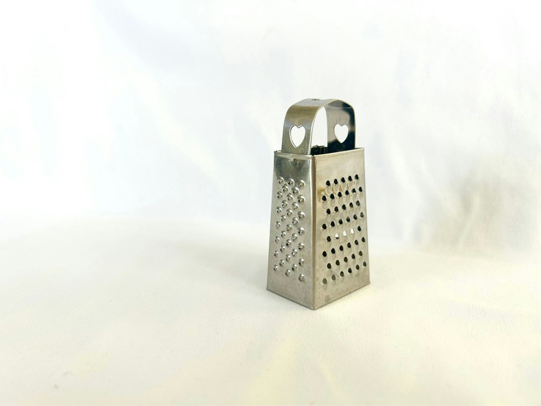 A small stainless box grater standing on a white counter