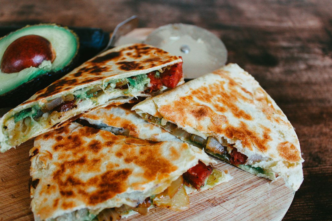 Quesadillas sliced into wedges on a wooden board with avocado