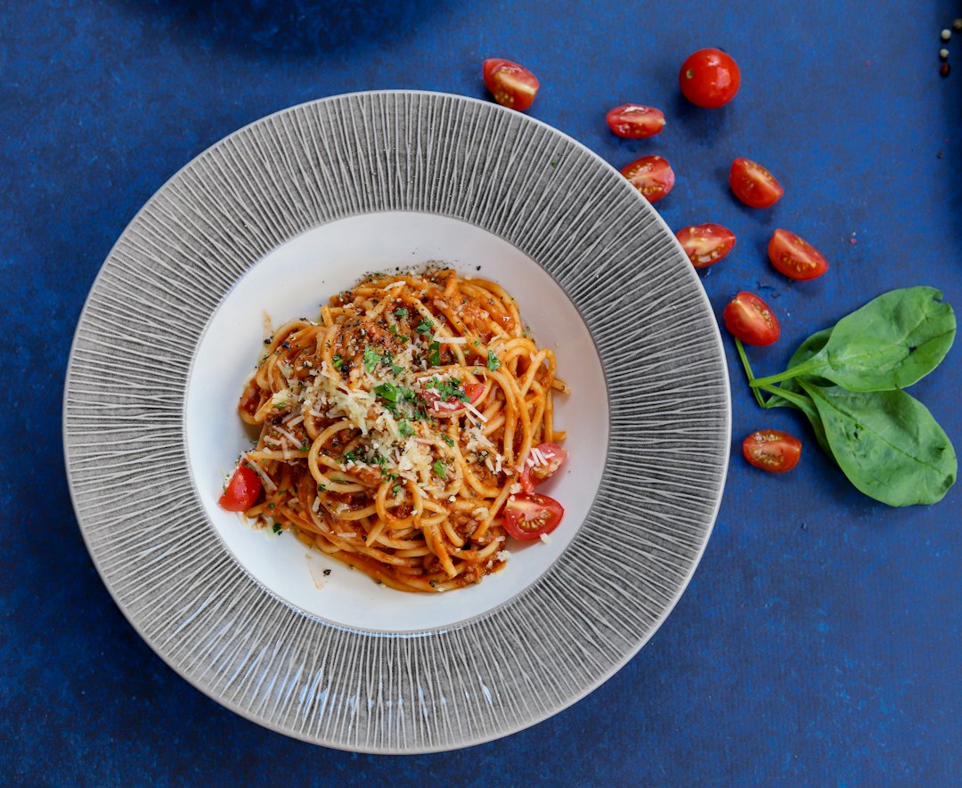 A bowl of tomato pasta finished with grated cheese, herbs, and cherry tomatoes