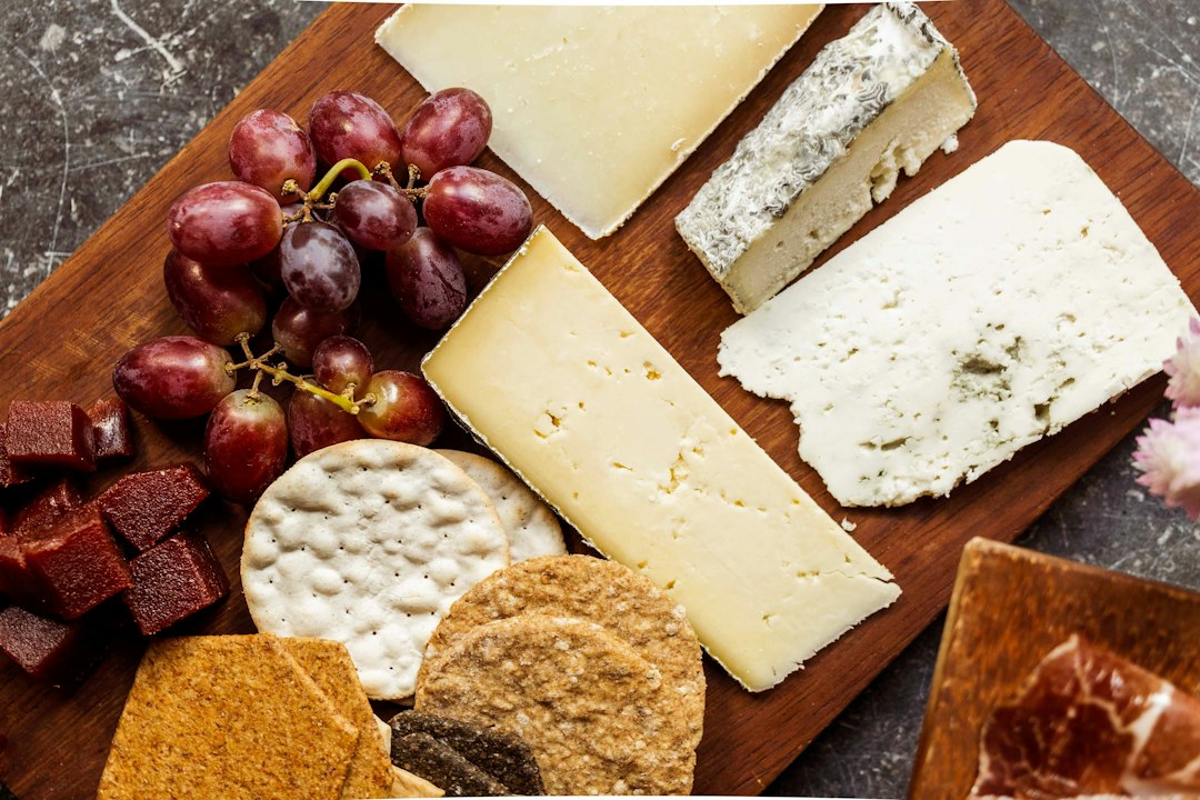 A wooden cheese board with grapes, crackers, and several styles of cheese