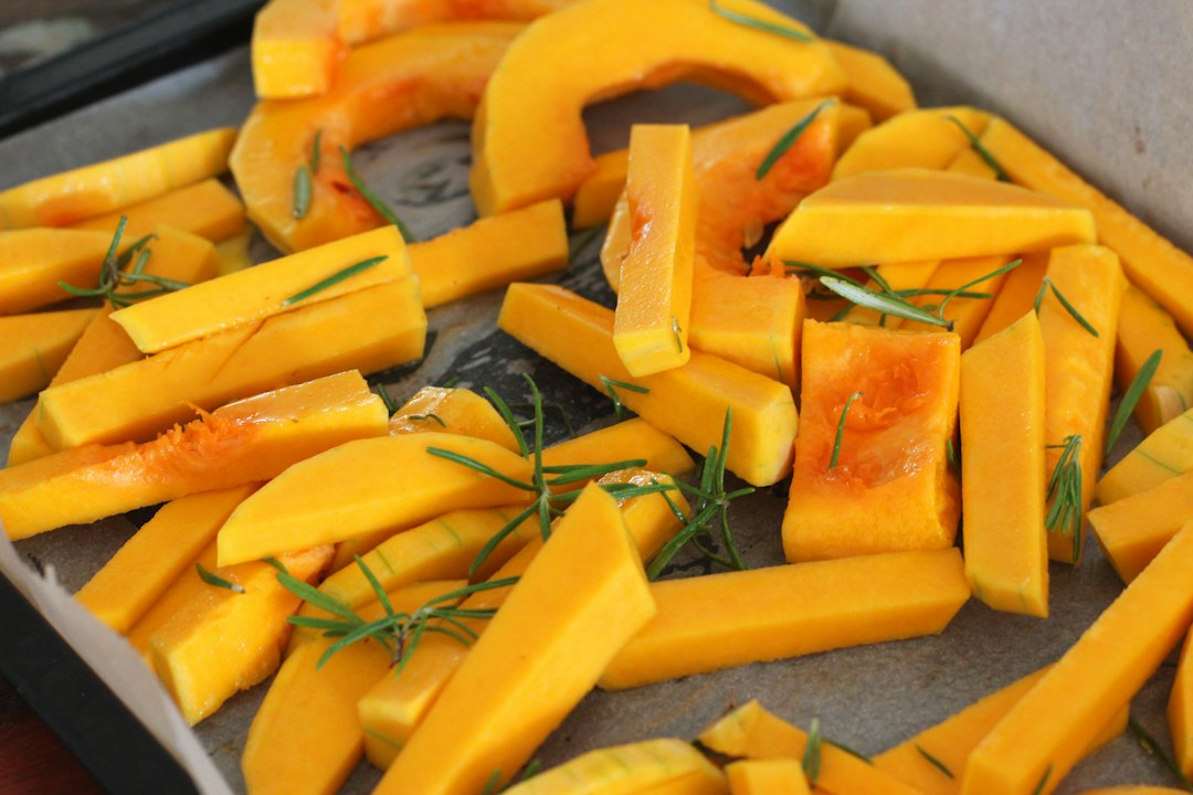 Raw butternut squash sticks and slices with fresh rosemary laid out on parchment, ready for roasting
